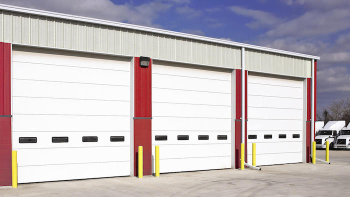 Row of heavy-duty white commercial steel sectional garage doors with vision lites at an Austin warehouse facility