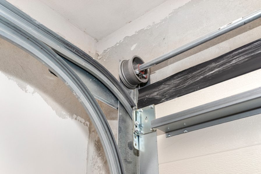 Detailed view of a garage door cable drum and steel track assembly in need of maintenance at an Austin home
