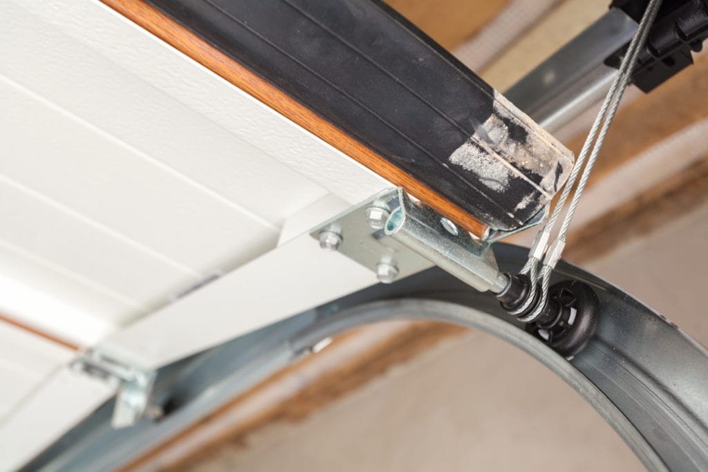 Close-up of a garage door nylon roller, steel cable, and track assembly being serviced in Austin
