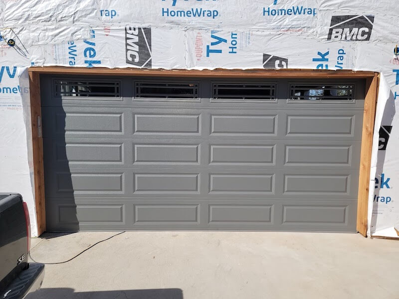 Charcoal gray raised panel garage door with decorative window inserts during a new home installation in Austin