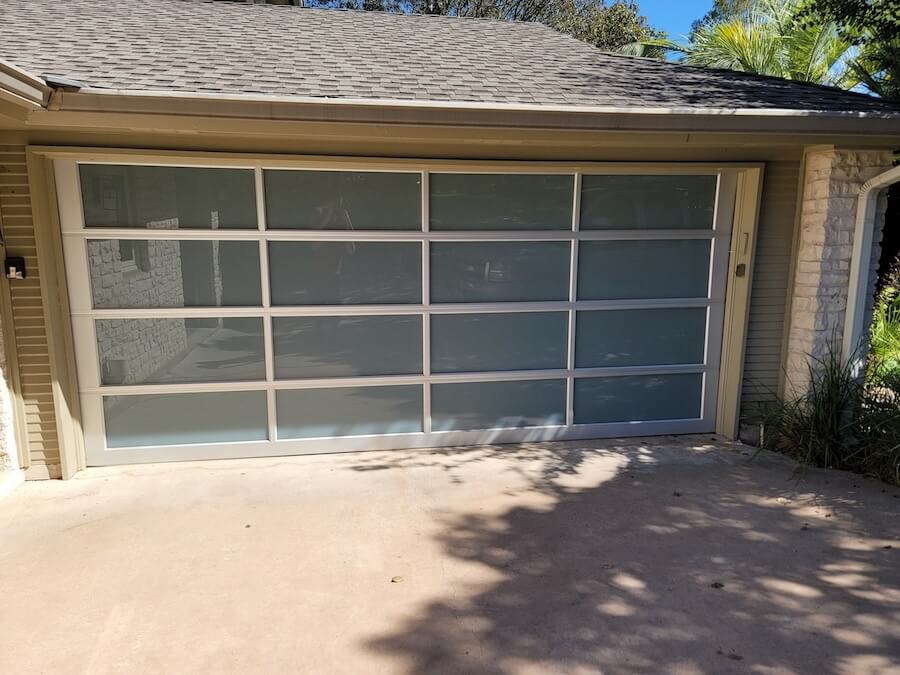 Contemporary full-view frosted glass and silver aluminum frame garage door installed on an Austin home